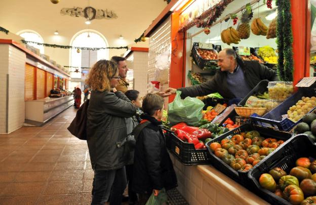 Una familia compra fruta y verdura en este puesto del mercado de abastos, ayer./ENRIQUE