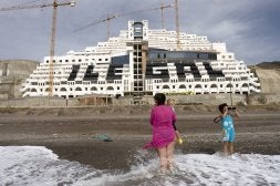 Una mujer y dos niños, en la playa de El Algarrobico, en Carboneras, con el hotel de Azata del Sol al fondo. /IDEAL/